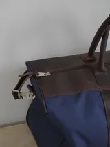 Bolso de lona color negro con detalles en cuero color tostado. Tiene doble asa de mano y correa de hombro ajustable y extraíble.