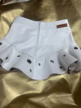Mini pollera blanca de cuero con volados y apliques metálicos circulares.