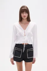 Blusa de rayón color blanco con detalles de broderie, cuello en V y cierre frontal con cordones para atar. Presenta mangas largas y cintura elástica con terminación en volado.