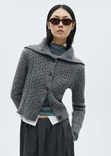 Cárdigan gris de tejido de punto grueso con diseño trenzado, cuello camisero, cierre frontal con botones y terminaciones acanaladas.