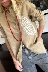 Camisa color beige de lino con bordado de caracol en el frente, de corte recto y manga larga.