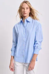 Camisa celeste a rayas verticales blancas, de manga larga con puños elásticos y volados en el frente.