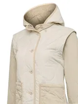 Campera beige acolchada con diseño de rombos, cierre con botones a presión, capucha y bolsillos delanteros. Las mangas son desmontables, transformándose en chaleco, y es reversible.