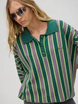 Chomba de corte oversize con cuello camisero, a rayas verticales en color marrón, lila y blanco. Tiene un logo bordado en el pecho y puños en color marrón.