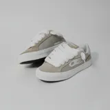 Zapatillas bajas de gamuza color beige y gris, con suela blanca y cordones gruesos blancos.
