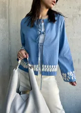 Chaqueta celeste con bordados florales blancos en el ruedo y los puños, con escote redondo y lazos para atar en el frente.