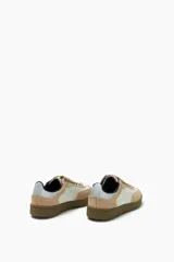 Zapatillas deportivas bajas color beige y blanco, con cordones y suela marrón.