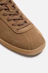 Zapatilla acordonada color marrón de piel serraje con pespuntes en el empeine y suela a tono.