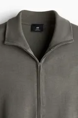 Cárdigan verde oliva de punto fino, con cuello polo y cierre bidireccional. Tiene corte ajustado y remate acanalado en cuello, puños y bajo.