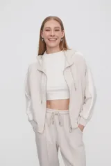 Campera con capucha color beige claro con cierre frontal y bolsillos laterales. Presenta una banda blanca en las mangas. Corte holgado.