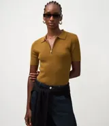 Blusa polo de punto color mostaza, ajustada al cuerpo, con cuello y manga corta. Presenta una cremallera frontal que llega hasta el escote.