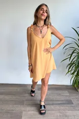 Vestido corto color amarillo mostaza, con escote en V y tirantes finos con detalle de volado o fruncido. El ruedo es asimétrico.