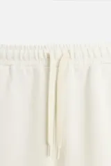 Pantalón negro de corte recto confeccionado en tejido interlock de algodón con elasticidad. Tiene cintura elástica ajustable con cordón, bolsillos frontales y bolsillos traseros de vivo.