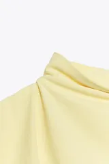 Vestido midi amarillo pálido, sin mangas, con cuello alto y detalle drapeado en el lateral.