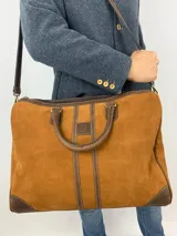 Bolso de mano confeccionado en cuero de color verde con detalles en marrón. Cuenta con dos asas superiores, una correa larga ajustable y removible, y cierre de cremallera. El diseño incluye franjas verticales decorativas en el centro y refuerzos en las esquinas inferiores.