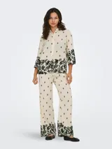 Pantalón de pierna ancha color crema con estampado de hojas negras, cintura elástica trasera y bolsillos frontales.