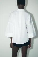 Camisa marrón de popelina con cuello solapa, escote en pico, cierre frontal con botones y mangas anchas con puños.