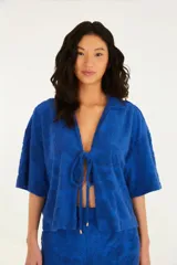 Camisa azul de toalla con cuello clásico, corte suelto, mangas cortas amplias y cierre con lazo.