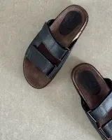 Sandalias bajas con base marrón y dos tiras anchas de cuero sintético negro con ajuste de velcro.