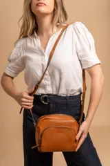 Bandolera de cuero sintético color beige, con diseño compacto y elegante. Cuenta con un bolsillo frontal con cierre y un compartimento principal con cierre. La correa es regulable.