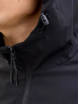 Campera softshell negra con capucha ajustable con cordón, mangas largas con puños de canalé, cierre frontal con cremallera y bolsillos delanteros. Forro sin relleno y costuras cubiertas.