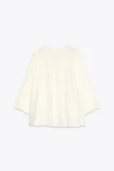 Blusa color crema de cuello redondo con escote pico y manga ancha por debajo del codo. Detalle de acabados con bordados. Cierre frontal con botones.