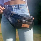 Riñonera negra con textura tipo piel de cocodrilo, con tres compartimentos con cierre y correa ajustable.