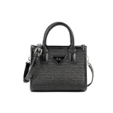Cartera chica negra con diseño en relieve, confeccionada en rafia y poliuretano. Tiene acceso con cierre, un bolsillo interno con cierre y otro abierto, correa regulable y asa fija.