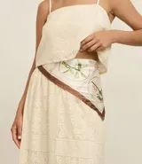 Pañuelo de poliéster satinado, color crema, con estampa botánica en tonos verdes y marrones, y bordes en color marrón oscuro.