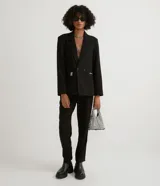 Blazer negro de poliéster y viscosa, de corte alargado, con cuello solapa, manga larga, doble botón frontal y bolsillos con solapa.