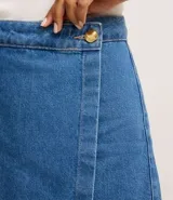 Short pollera de jeans azul de cintura alta, con diseño de traspase tipo sobre abrochado con un botón dorado.