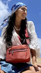 Bandolera color rosa viejo con detalles en cuero marrón claro, múltiples cremalleras metálicas y herrajes plateados. Incluye correa ancha ajustable con el logo de la marca.