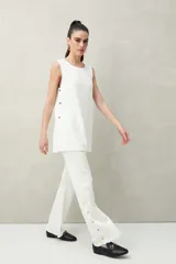 Pantalón blanco de punto con calce relajado y caída fluida. El detalle de botones dorados en los laterales aporta un toque distintivo y moderno.