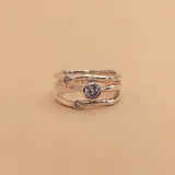 Anillo de plata 925 satinada con tres aros y tres circonias engarzadas. El aro superior tiene una circonia pequeña, el aro central tiene una circonia más grande y el aro inferior tiene una circonia pequeña.