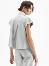 Camisa de cuero ovino negra, con volados en el centro delantero, mangas con volumen fruncidas en la copa y broches forrados en cuero.