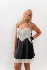 Camisón corto negro de satén con breteles finos y escote en V con puntilla blanca.