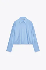Camisa celeste de algodón con corte crop, cuello solapa, mangas largas con puños y cierre frontal con botones ocultos.