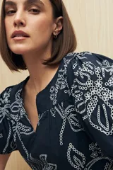 Blusa azul marino con bordados y calados blancos, escote en pico y mangas abullonadas con puño elastizado.