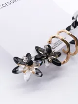 Set de tres pares de aros con diferentes diseños: aros tipo botón con forma de flor en blanco y negro, aros colgantes dorados con forma de onda y aros tipo argolla con estampado abstracto en blanco y negro.