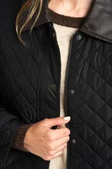 Campera capitoneada de color negro con diseño de rombos, cuello camisero en contraste de color marrón, cierre frontal con cremallera y solapa con botones a presión. Presenta mangas largas con puños ajustables y un calce entallado.