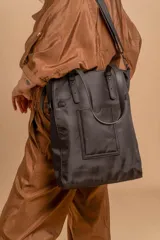 Cartera tipo tote bag color negro, con doble asa de mano y correa bandolera ajustable. Presenta un bolsillo rectangular en el frente.