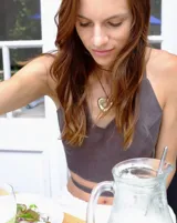 Collar con dije dorado irregular con agujero central, colgando de cordón negro ajustable.