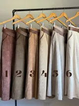 Falda midi de corderoy color beige claro, con pliegues verticales marcados y cintura elastizada. Incluye un cinturón desmontable de cuero marrón con hebilla dorada.