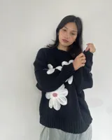 Sweater tejido negro con cuello redondo y tres flores blancas bordadas en el frente.