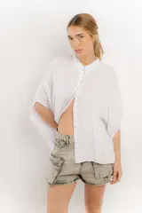 Camisa celeste de lino con corte amplio, cuello mao y mangas cortas. Presenta cierre frontal con botones y ribete negro en cuello y tapeta.