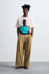 Camiseta color crema de corte holgado con cuello redondo y mangas cortas. Estampado frontal con la ilustración de un hombre sentado en un sillón.