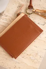 Porta celular de cuero vegano, con diseño combinado en tonos marrón y dorado, incluyendo un llavero con borlas.
