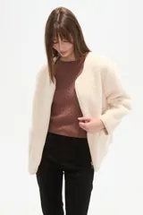 Chaqueta corta de tejido bouclé o pelo sintético color crema, con cuello redondo, cierre frontal metálico y dos bolsillos frontales amplios.