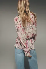 Camisa semitransparente con estampado de flores en tonos rosa y verde, cuello pico y manga larga con puños. Tiene aberturas laterales y cierre frontal con botones.