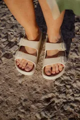 Sandalias tipo ojotas color beige con dos tiras anchas con hebillas ajustables.